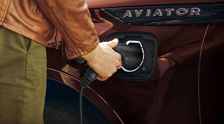 A hand is shown plugging a charger into the charging port of a 2023 Lincoln Aviator® Plug-in Hybrid model. | Astro Lincoln in Pensacola FL